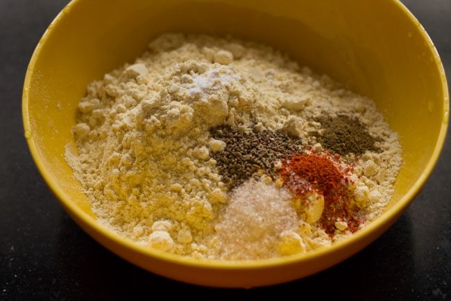 gram flour, baking powder, carom seeds, spice powders and salt added in a bowl. 