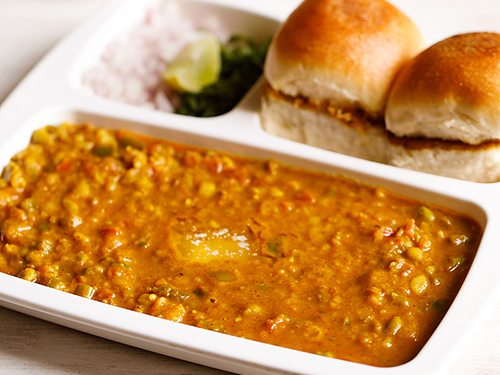 pav bhaji in a tray with pav, onions and lemon.