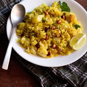 batata poha on a white plate with lemon wedge on right side and a spoon on the left side.