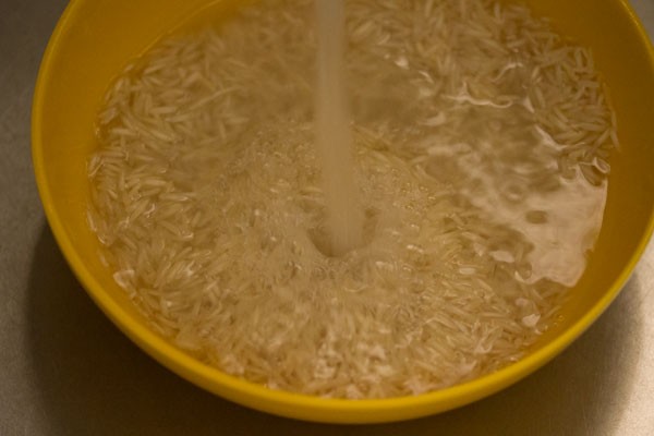 basmati rice being rinsed in running water. 