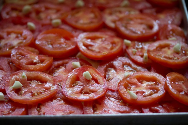 sliced tomatoes and rough chopped garlic on a sheet pan for roasting.