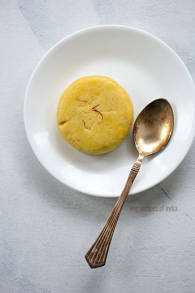badam halwa served on a white plate with a brass spoon by the side