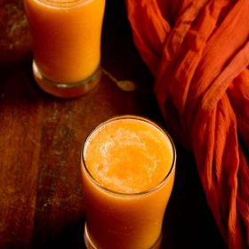 cantaloupe juice or muskmelon juice in two tall clear glasses on a wooden table next to an orange piece of fabric