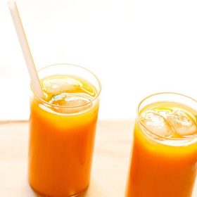 mango tea in two glasses with ice cubes and a straw in one glass