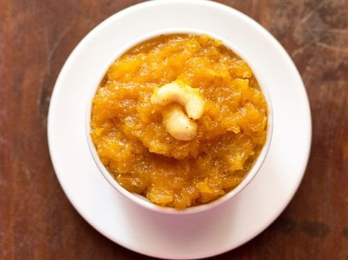 papaya halwa garnished with cashews and served in a white bowl kept on a white plate.