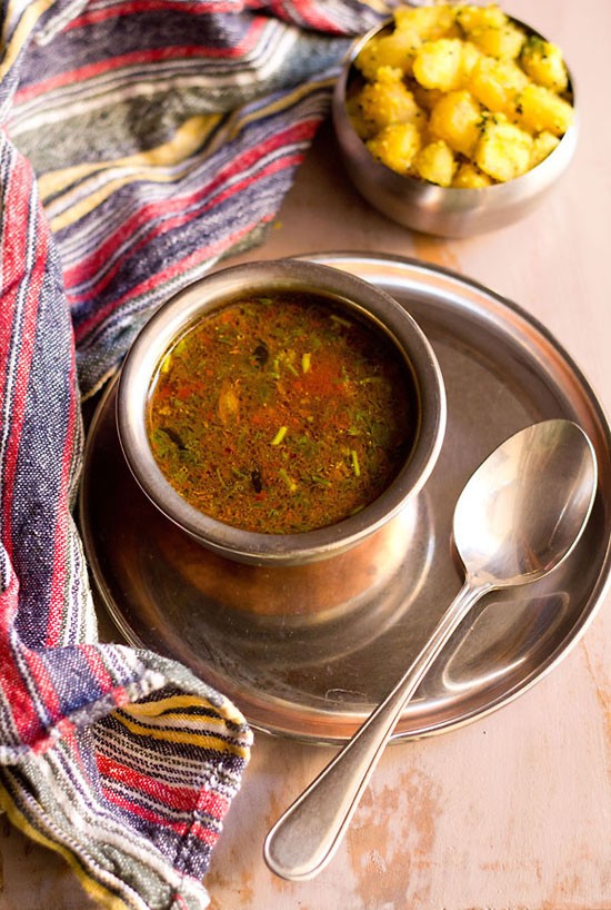 jeera milagu rasam served in a steel bowl with a spoon kept on the right side.
