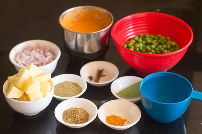 ingredients for making potato peas kurma recipe measured out in dishes on a black tabletop.