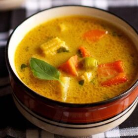 thai yellow curry served in a black rimmed ceramic bowl with a bowl of steamed rice kept in the background.