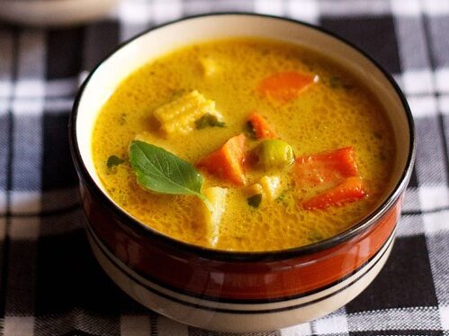 thai yellow curry served in a black rimmed ceramic bowl with a bowl of steamed rice kept in the background.