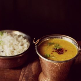 lasooni dal tadka garnished with coriander leaves and served in a copper bowl with a side of steamed rice and text layover.