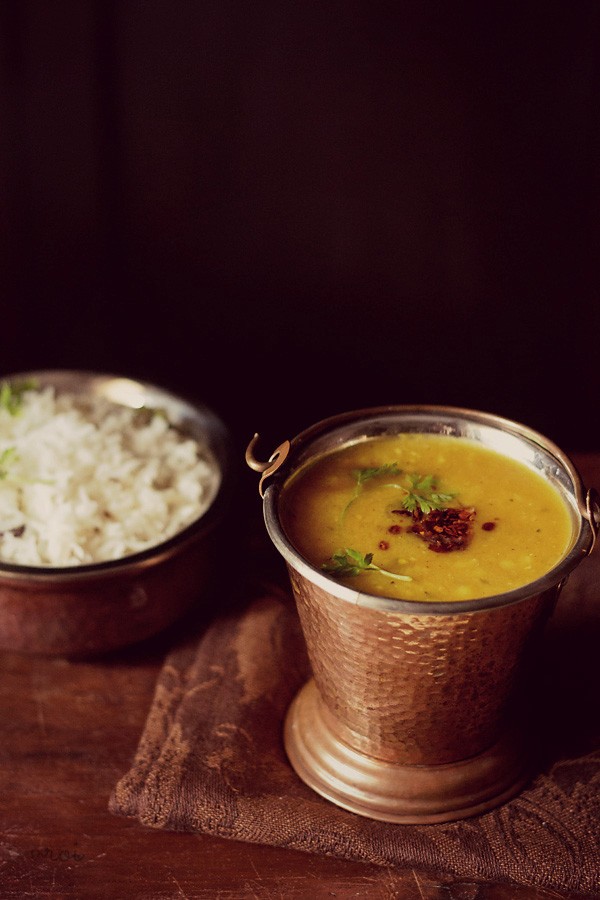lasooni dal tadka garnished with coriander leaves and served in a copper bowl with a side of steamed rice and text layover.