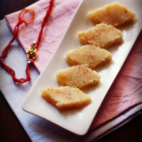 Coconut burfi slices on white plate with rakhi in background.