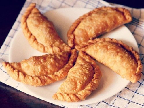 gujiya arranged neatly on a white plate placed on a white and blue checkered napkin.