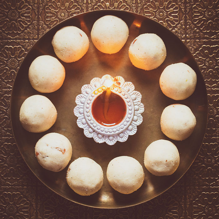 rava ladoo in a circle with lit earthern lamp in center on a bronze plate.