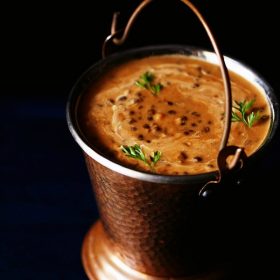 dal makhani served in a copper bucket and garnished with three cilantro sprigs