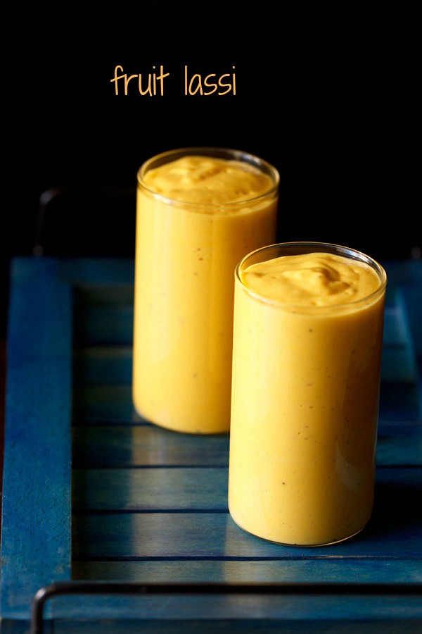 two glasses filled with fruit lassi on a dark blue tray.