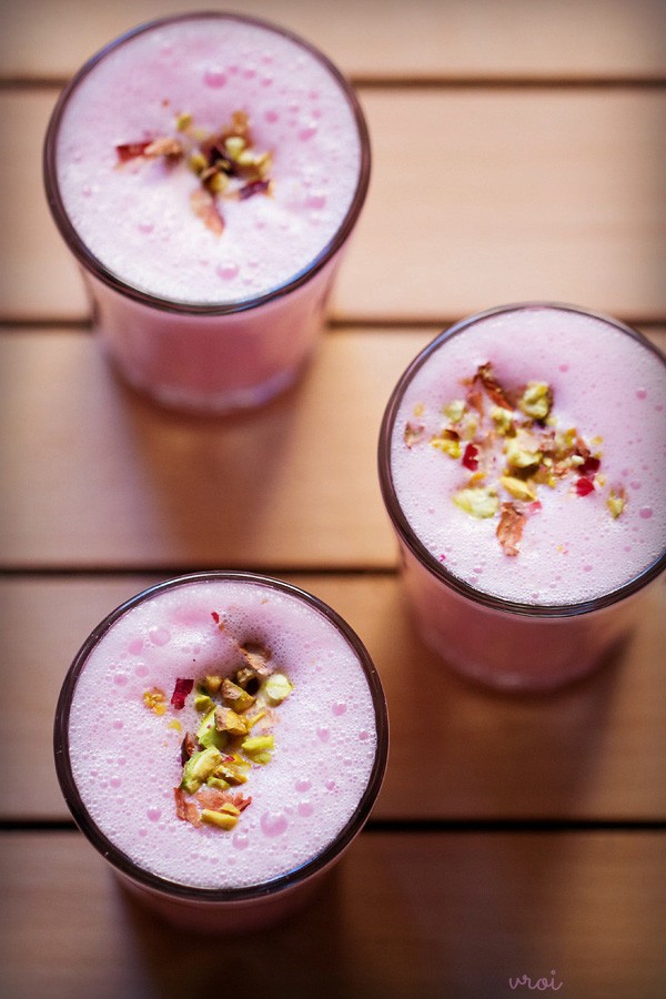 top shot of rose lassi garnished with chopped nuts, dried rose petals and served in 3 glasses. 