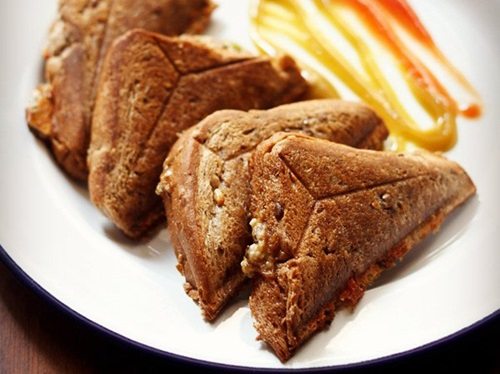 four bell pepper sandwich triangles served on a white plate with tomato ketchup and chili sauce.