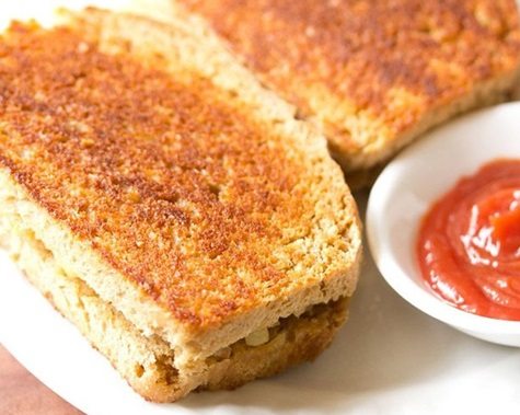 tawa sandwich served on a white plate with a small bowl of tomato ketchup kept on the side.