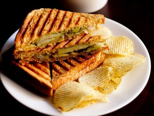 grilled sandwich with potato wafers on a white plate.