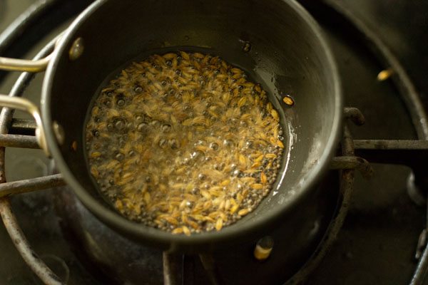 cumin seeds crackling and sizzling in black tadka pan. 