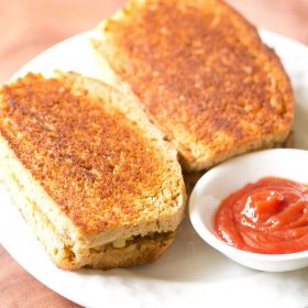 tawa sandwich served on a white plate with a small bowl of tomato ketchup kept on the side.