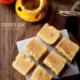 Mysore pak cubes are placed on a wooden tray on the table.