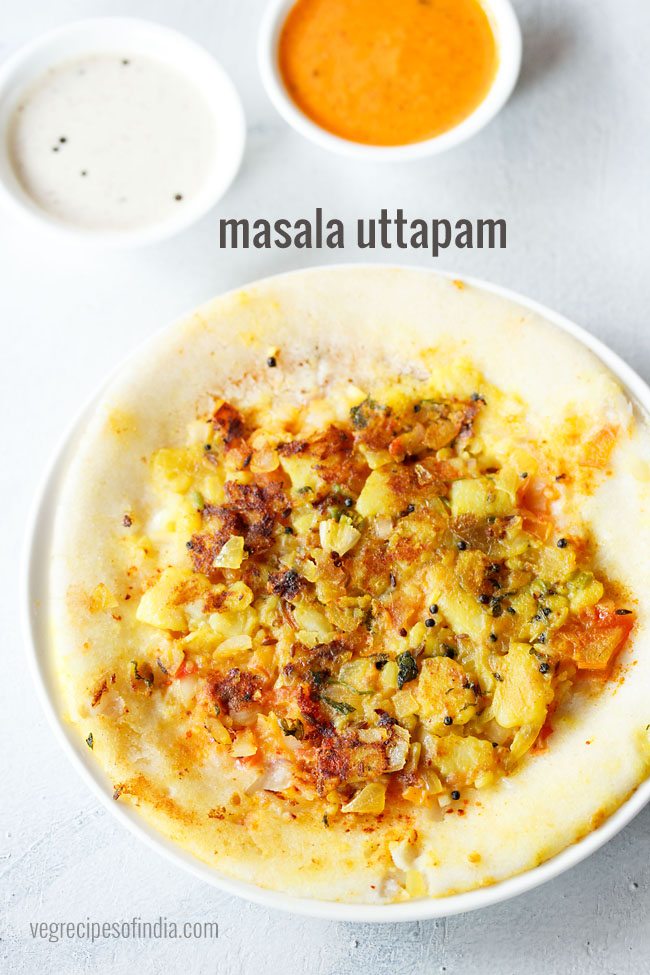 masala uttapam on a white plate with sides of red coconut chutney and white coconut chutney.