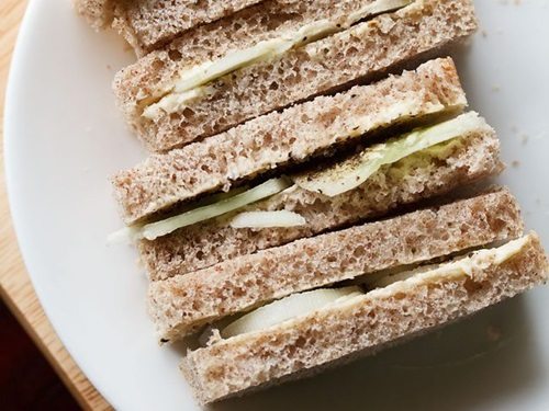 close up shot of stacked cucumber sandwiches with the visible layers of cucumber and bread placed on a white plate