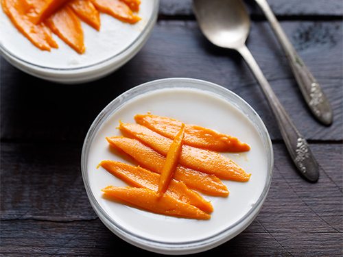 panna cotta in a bowl garnished with mango slices.