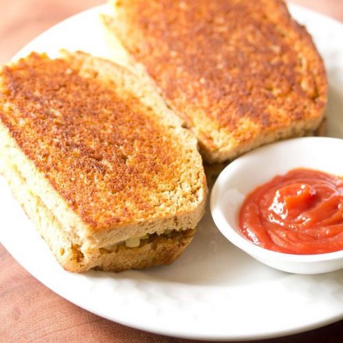 tawa sandwich served on a white plate with a small bowl of tomato ketchup kept on the side.