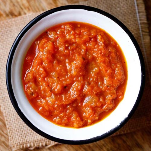 overhead shot of homemade marinara in a white bowl with a black rim on a piece of burlap.