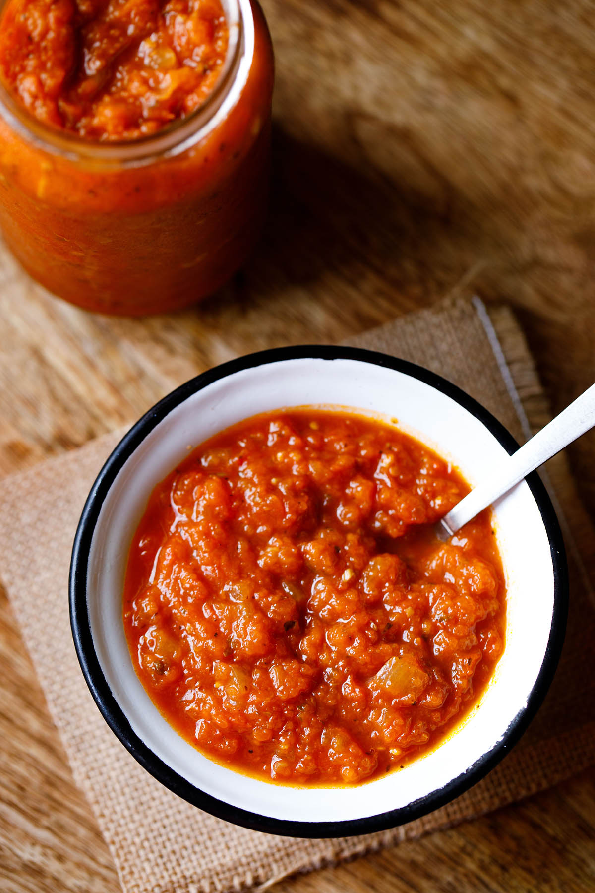 glass jar filled with homemade marinara next to bowl with silver spoonful of marinara.