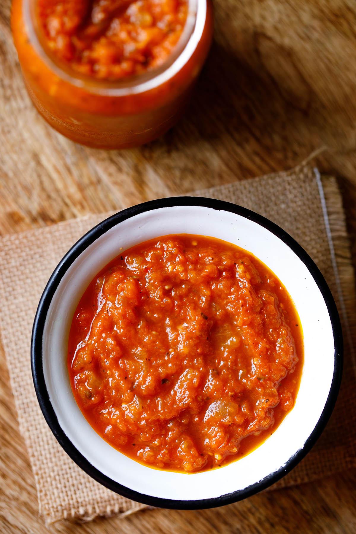 overhead shot of homemade marinara in a white bowl with a black rim on a piece of burlap.