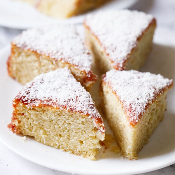 vanilla cake triangular wedges topped with jam icing and desiccated coconut on a white plate