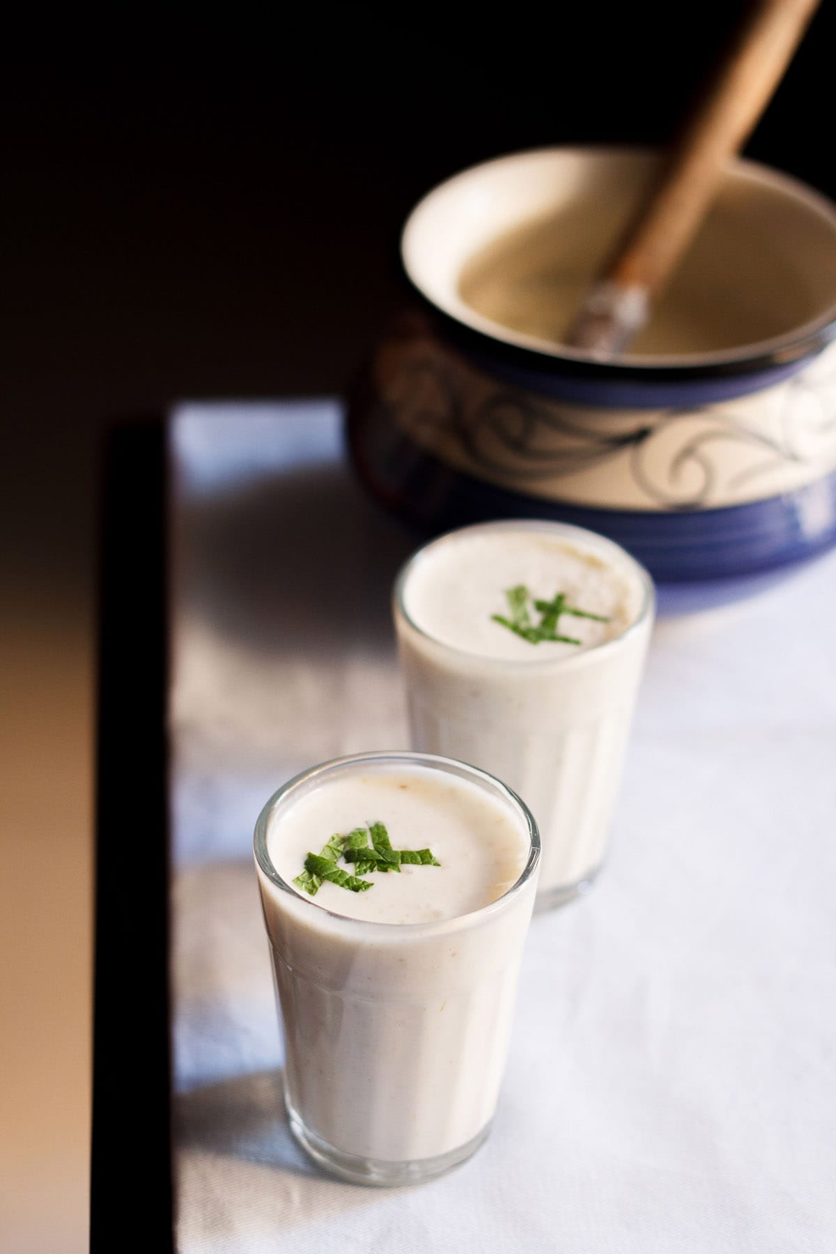 salted lassi topped with chopped mint in two small glasses on a wooden table lined with light blue linen