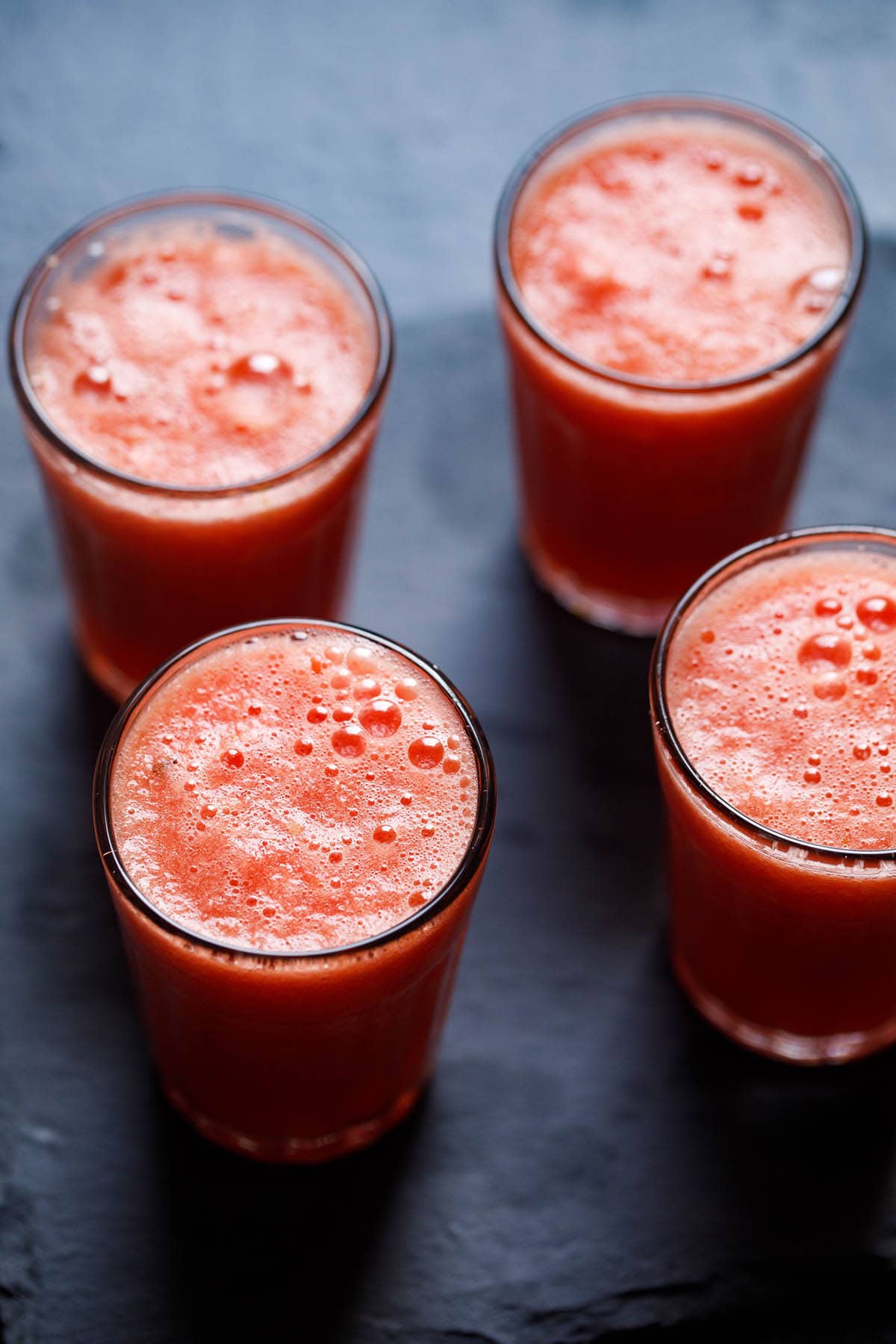 4 glasses of watermelon juice on a dark slate serving plate