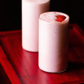 strawberry milkshake topped with strawberry slices in two glasses on a reddish pink tray