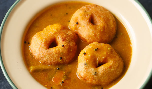 medu vada sambar in a beige colored shallow plate.