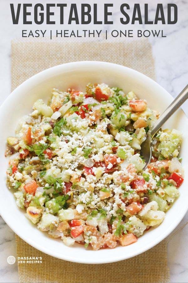 top shot of vegetable salad topped with crumbled feta and parsley with a spoon in a white bowl with text layovers