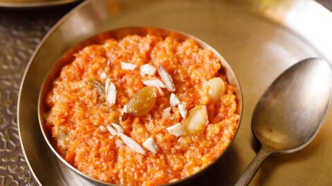 gajar ka halwa in a bronze bowl on a bronze plate with a bronze spoon by side