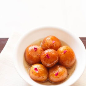 gulab jamun served in a white bowl on a white napkin.