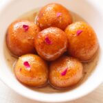 closeup image of gulab jamun served in a white bowl on a white napkin.