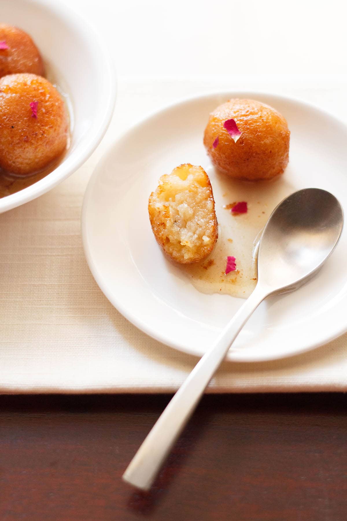 gulab jamun halved with a spoon on white plate.