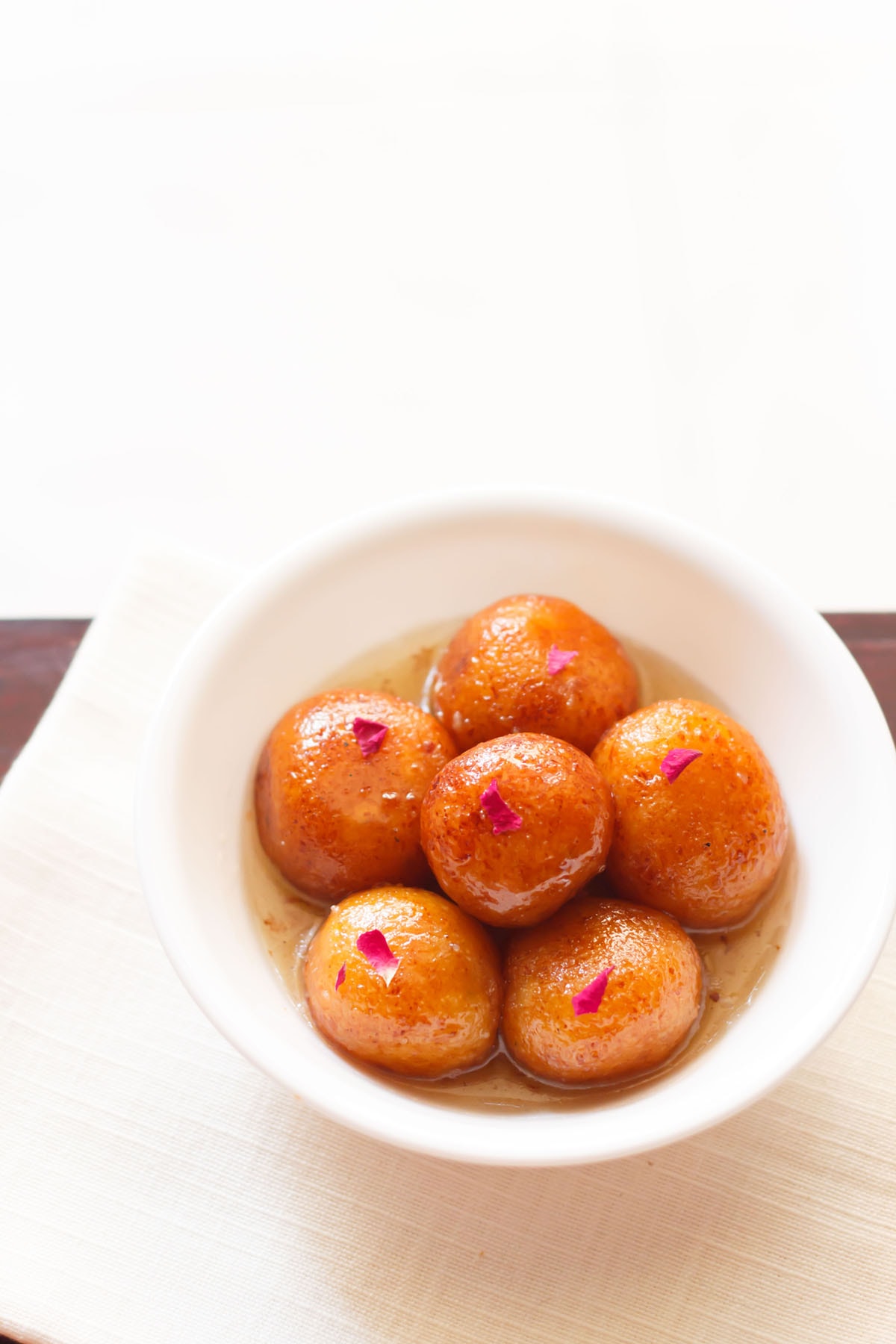 gulab jamun served in a white bowl on a white napkin.