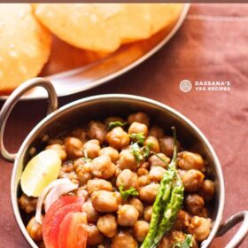 chana masala in a small serving wok topped with sliced tomatoes, onions, lemon and green chillies served with poori with text layovers.