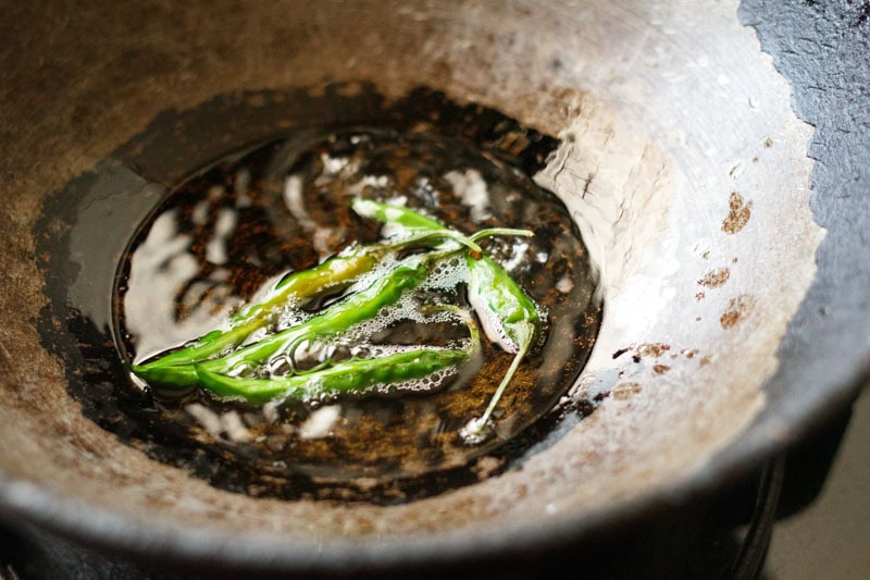 green chillies getting fried in oil in a wok.