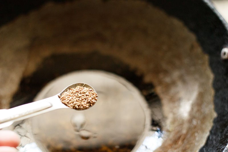 carom seeds in a small measuring spoon being added to oil in wok.