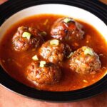 manchurian gravy garnished with chopped spring onion greens and served in a black rimmed bowl.