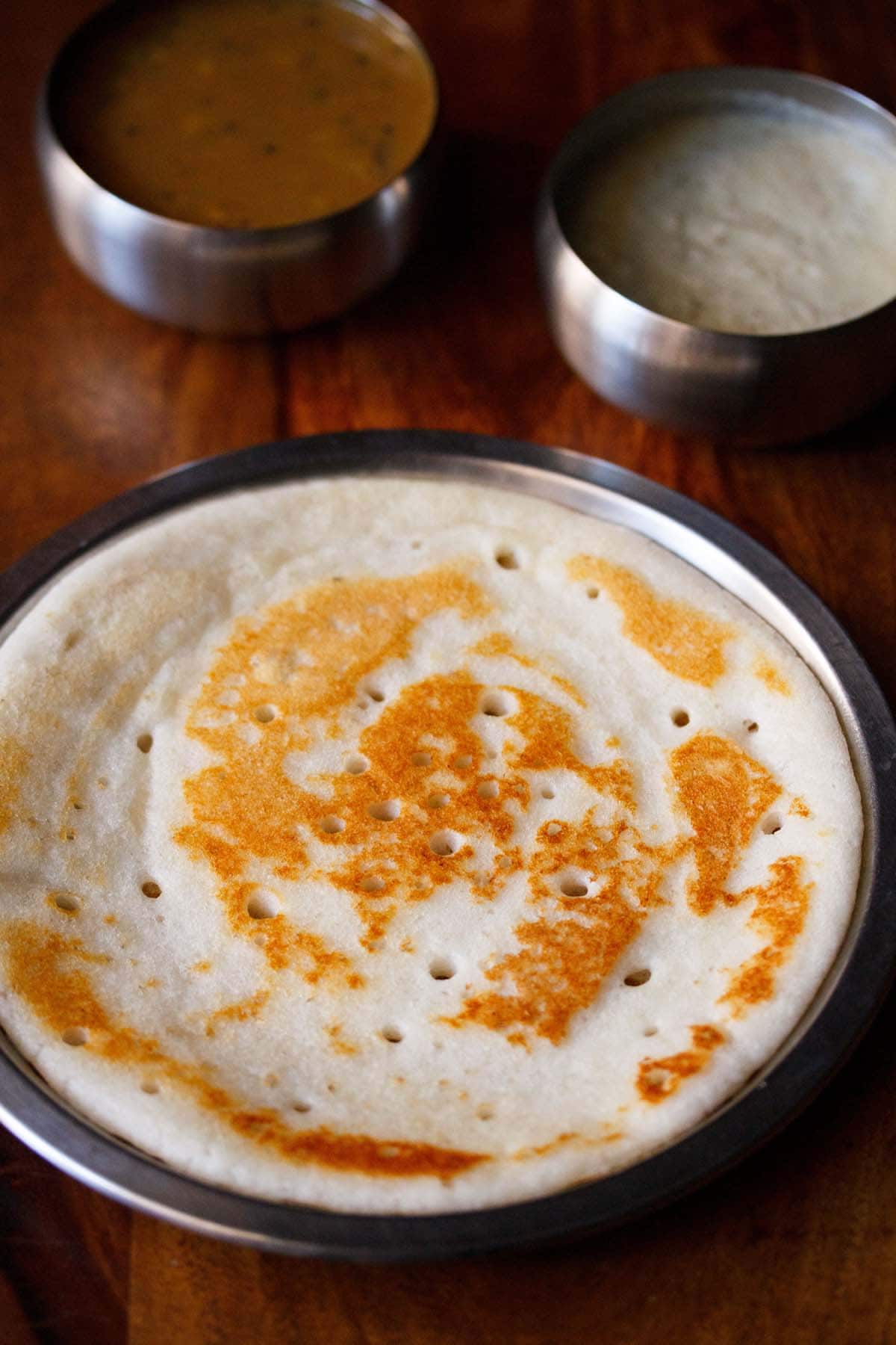 uthappam served on a steel plate with a side of coconut chutney and sambar. 